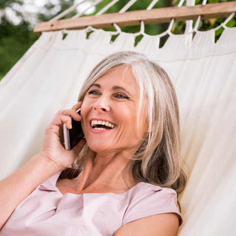 Older woman on her cell phone smiling in a hammock