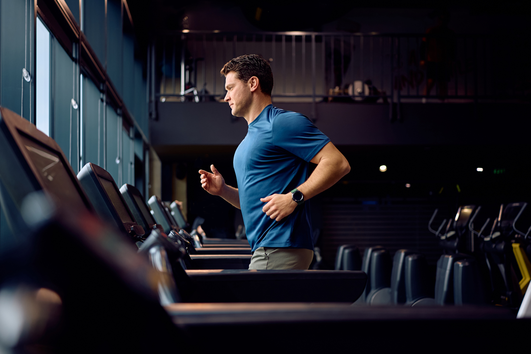 Mid adult sportsman running on treadmill at health club.